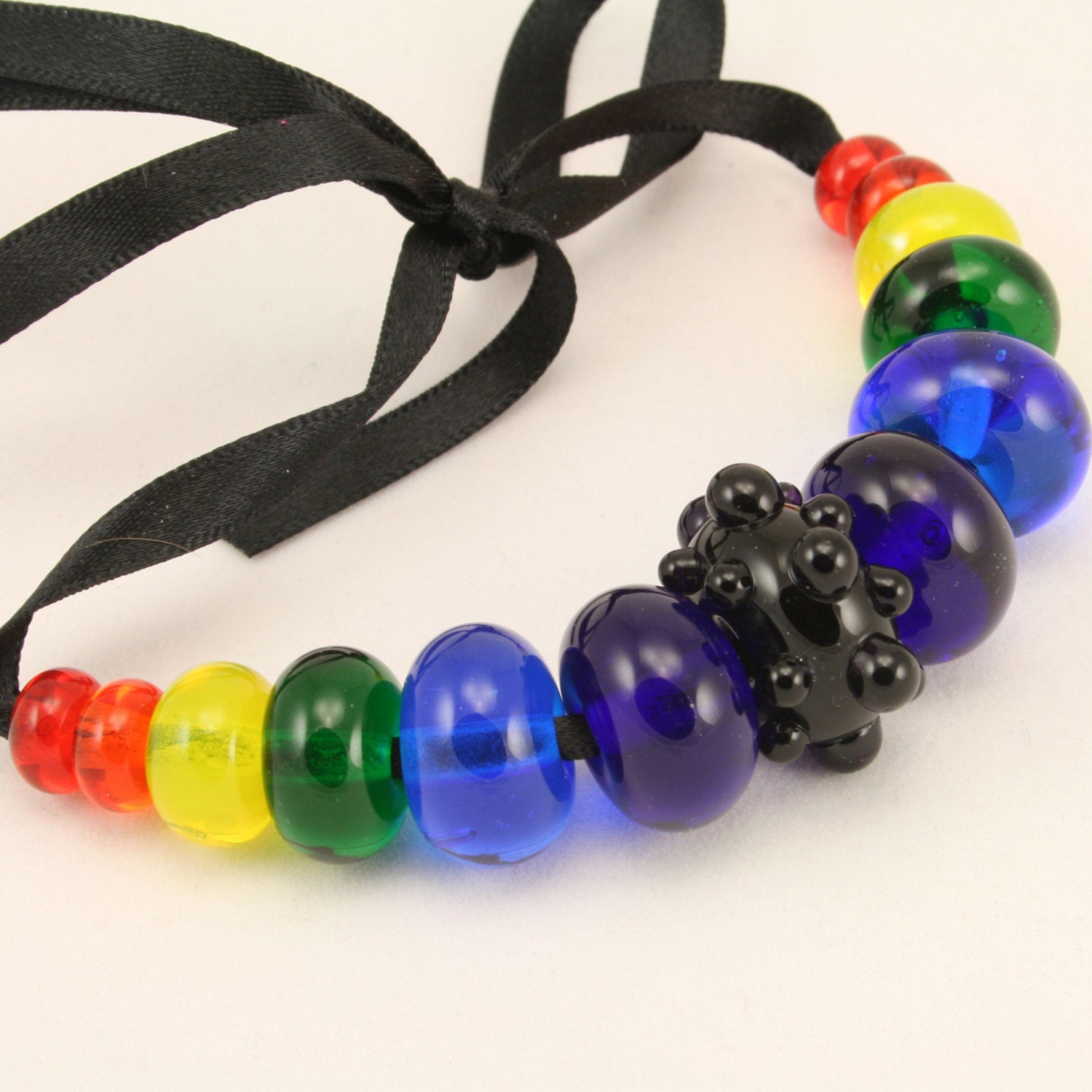A Graduated set of 13 lampwork glass beads in a Rainbow of transparents, with a deep violet bumpy focal bead.