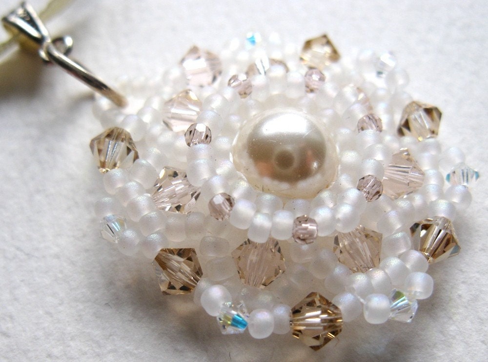 A delicate pendant handwoven from seed beads and crystals, with a glass pearl at its heart.